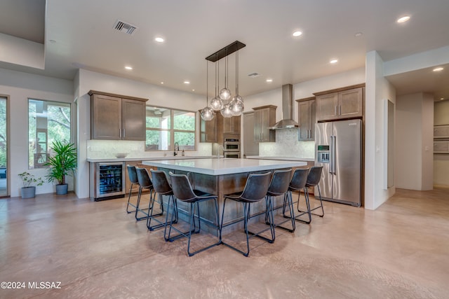 kitchen featuring wall chimney exhaust hood, a spacious island, beverage cooler, appliances with stainless steel finishes, and a healthy amount of sunlight