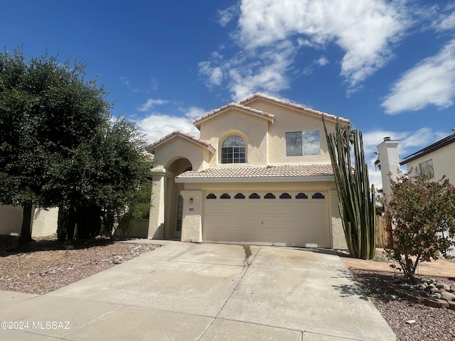 mediterranean / spanish house with a garage, driveway, a tile roof, and stucco siding