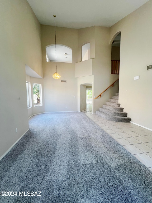 unfurnished living room featuring a towering ceiling, a healthy amount of sunlight, and light carpet