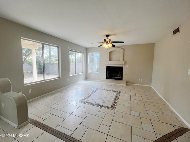 unfurnished living room with light tile patterned floors, visible vents, baseboards, a fireplace with raised hearth, and ceiling fan