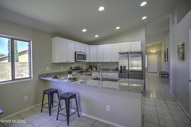 kitchen with vaulted ceiling, a peninsula, white cabinetry, stainless steel appliances, and a sink