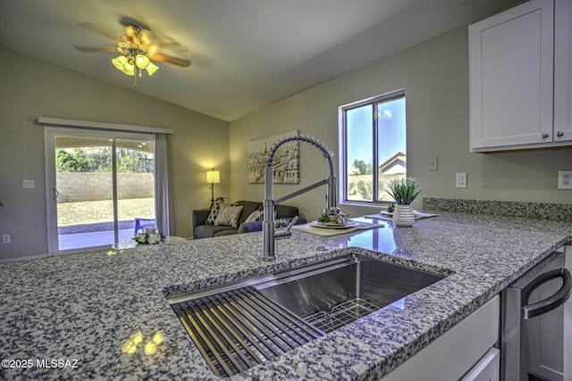 kitchen featuring dishwashing machine, vaulted ceiling, a sink, and light stone counters