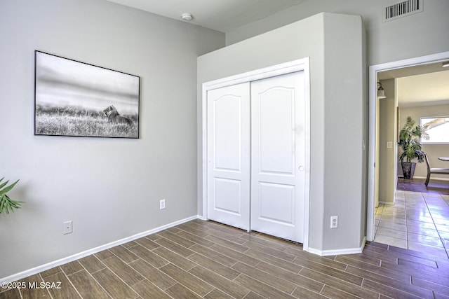 unfurnished bedroom featuring dark wood-type flooring, visible vents, baseboards, and a closet