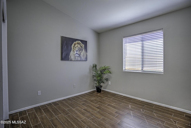 spare room featuring dark wood-style flooring, baseboards, and vaulted ceiling
