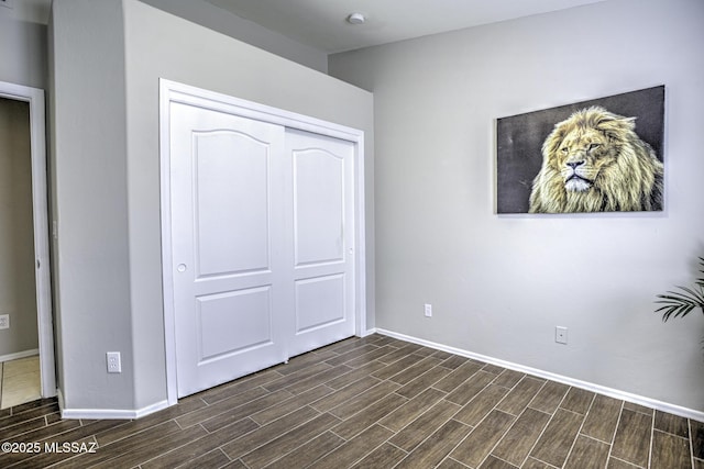 unfurnished bedroom with a closet, baseboards, and dark wood-style floors