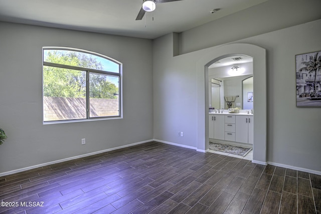 unfurnished room featuring arched walkways, ceiling fan, baseboards, and dark wood-style floors