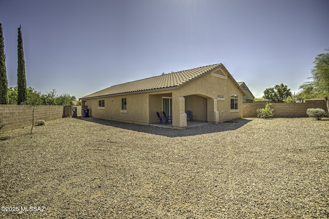 back of property with a fenced backyard, a tile roof, a patio, and stucco siding