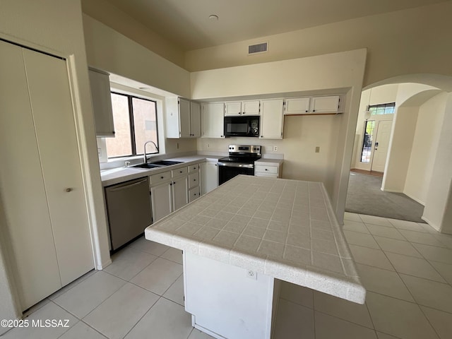 kitchen with sink, appliances with stainless steel finishes, white cabinetry, a center island, and tile counters