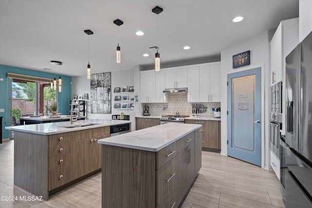 kitchen featuring a center island with sink, white cabinets, decorative light fixtures, stainless steel appliances, and under cabinet range hood