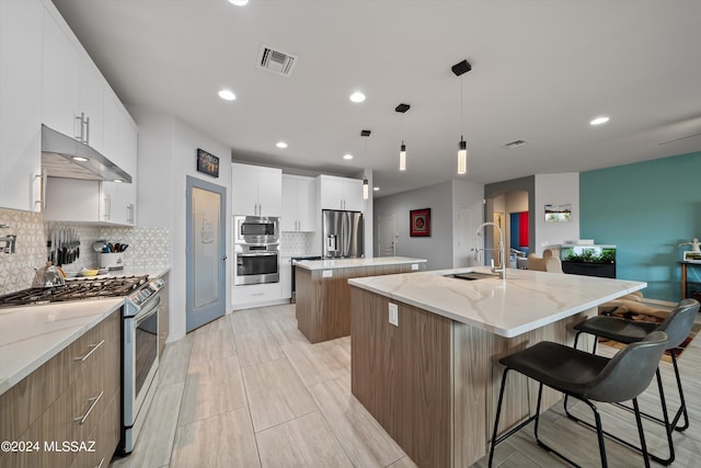 kitchen with stainless steel appliances, pendant lighting, white cabinets, and a center island with sink