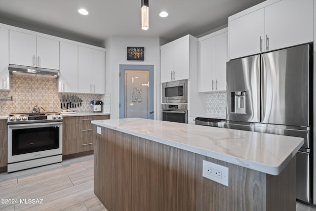 kitchen with decorative light fixtures, stainless steel appliances, white cabinetry, light stone countertops, and under cabinet range hood