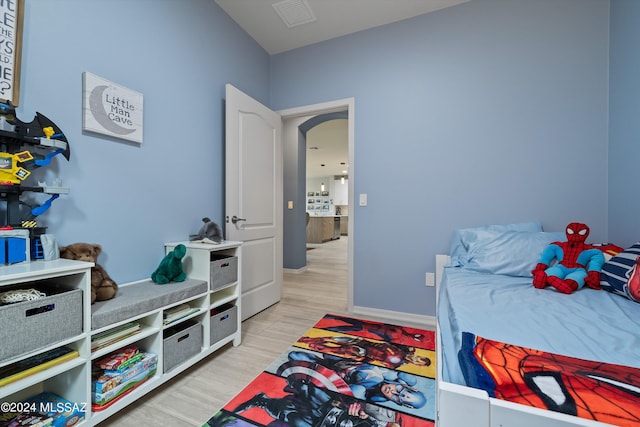 bedroom featuring light wood-type flooring, arched walkways, visible vents, and baseboards