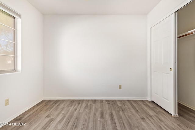unfurnished bedroom featuring baseboards, a closet, wood finished floors, and multiple windows