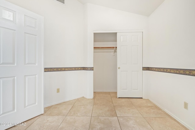 unfurnished bedroom featuring tile patterned flooring, baseboards, a closet, and vaulted ceiling