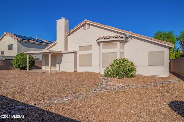 view of side of property featuring a tile roof, a chimney, stucco siding, fence, and a patio