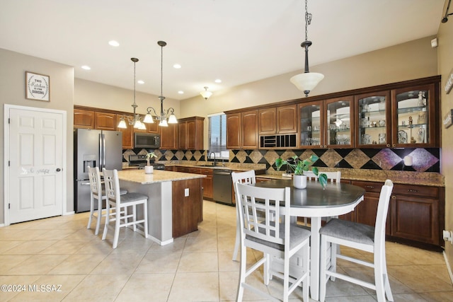 kitchen with hanging light fixtures, light tile patterned floors, a kitchen island with sink, backsplash, and appliances with stainless steel finishes