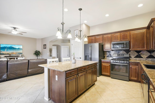 kitchen featuring pendant lighting, light stone counters, a kitchen island, backsplash, and appliances with stainless steel finishes