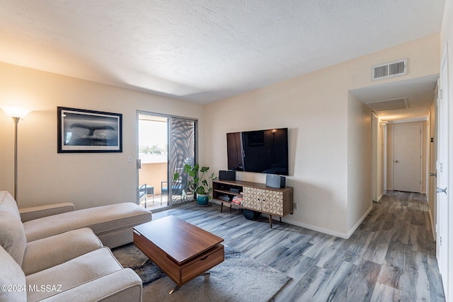 living room with visible vents, a textured ceiling, baseboards, and wood finished floors