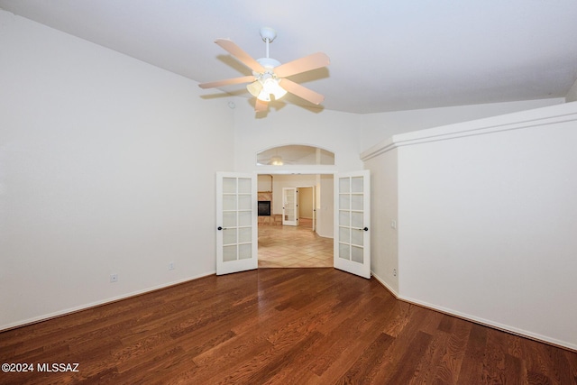 empty room featuring arched walkways, french doors, a ceiling fan, baseboards, and wood finished floors