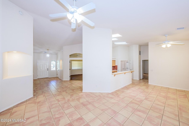 unfurnished living room featuring ceiling fan, visible vents, vaulted ceiling, light tile patterned floors, and baseboards