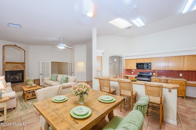 dining space with a fireplace, a ceiling fan, light tile patterned floors, lofted ceiling, and visible vents