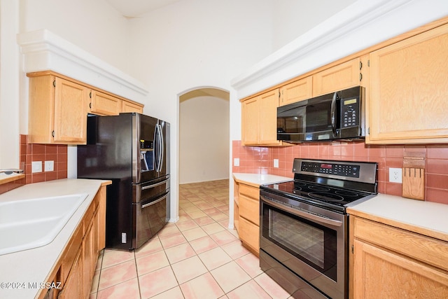 kitchen with arched walkways, appliances with stainless steel finishes, a sink, and light brown cabinets