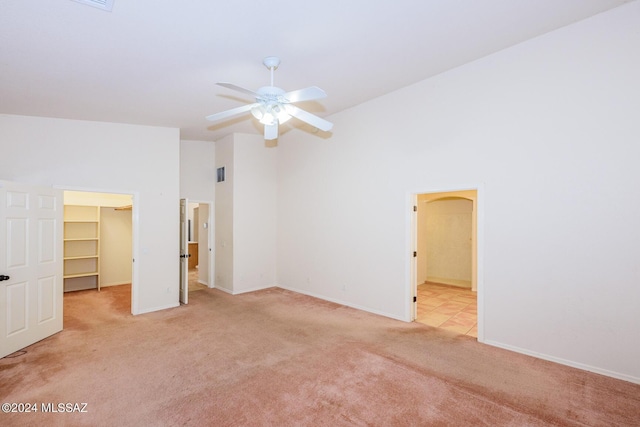 unfurnished bedroom featuring a walk in closet, baseboards, light carpet, and lofted ceiling
