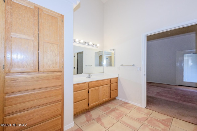 bathroom with vanity, tile patterned flooring, baseboards, and a towering ceiling