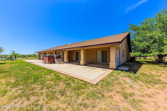 rear view of house with a jacuzzi, a patio, stucco siding, and a yard