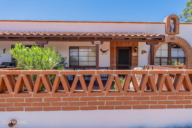 view of front facade featuring a tiled roof, a porch, a fenced front yard, and stucco siding