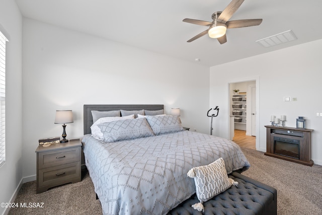 bedroom featuring a spacious closet, a closet, ceiling fan, and light colored carpet