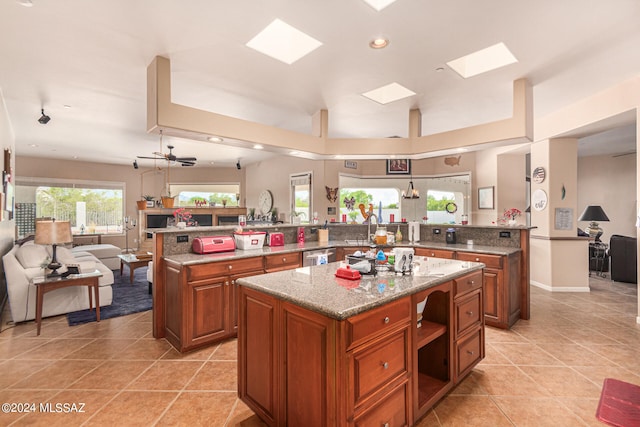 kitchen with dark stone countertops, a skylight, light tile patterned floors, kitchen peninsula, and a center island