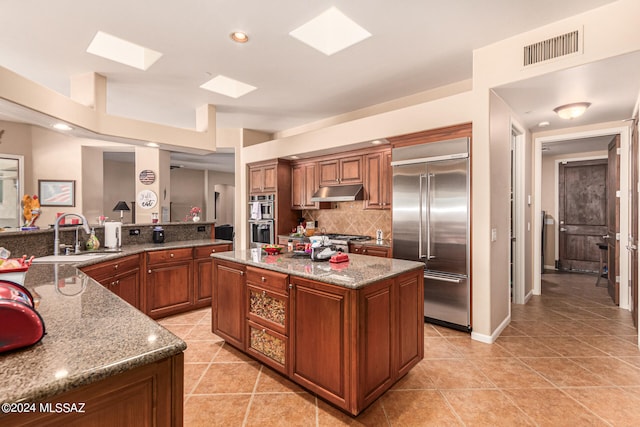 kitchen with a kitchen island, light stone countertops, stainless steel appliances, sink, and decorative backsplash