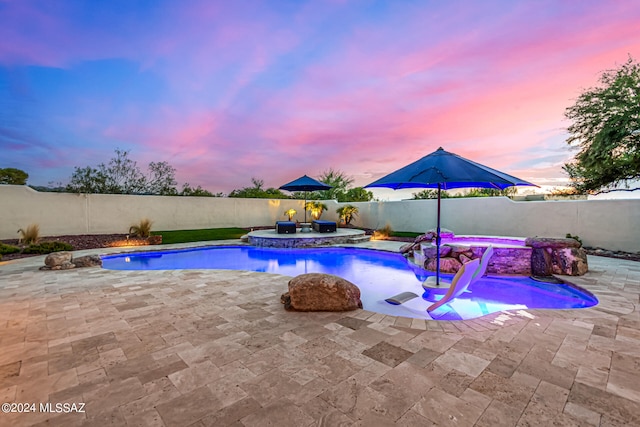 pool at dusk with a hot tub, a patio, and pool water feature