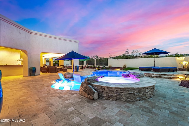 pool at dusk with a patio area and an in ground hot tub