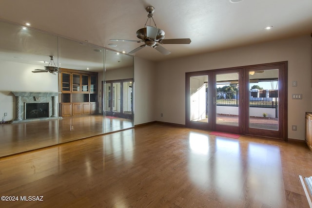 unfurnished living room featuring baseboards, a ceiling fan, wood finished floors, and a high end fireplace