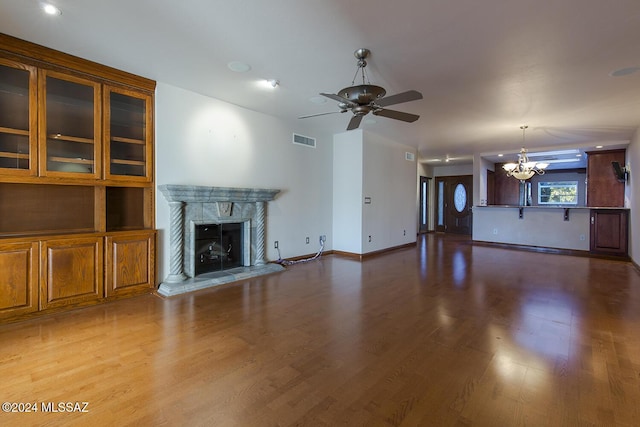 unfurnished living room featuring visible vents, baseboards, a premium fireplace, ceiling fan with notable chandelier, and wood finished floors