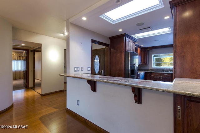 kitchen with visible vents, wood finished floors, stainless steel fridge, a skylight, and light stone countertops