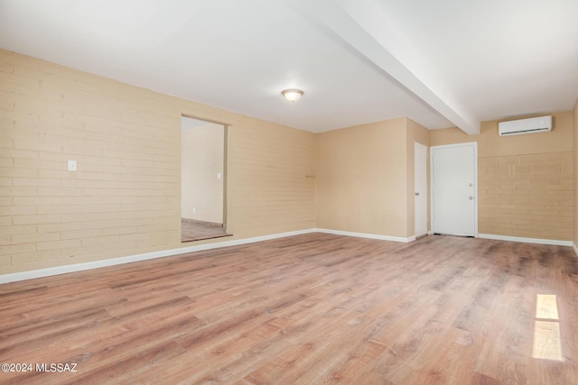 empty room with a wall mounted AC, light hardwood / wood-style flooring, and beamed ceiling