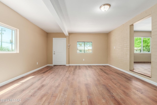 unfurnished room featuring brick wall, light hardwood / wood-style floors, and beamed ceiling