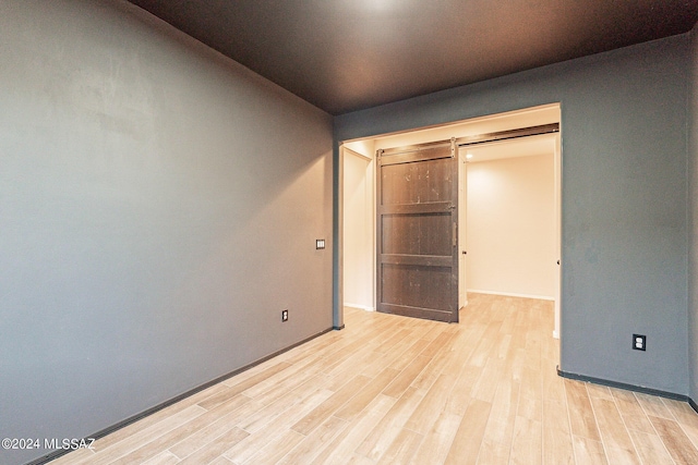 unfurnished bedroom with light wood-type flooring and a barn door