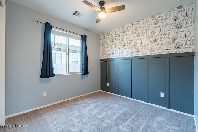 carpeted empty room featuring a wainscoted wall, ceiling fan, visible vents, and a decorative wall