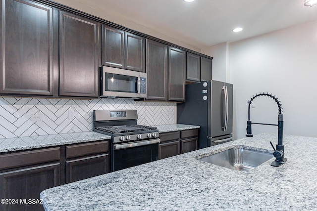 kitchen with a sink, dark brown cabinets, appliances with stainless steel finishes, backsplash, and light stone countertops