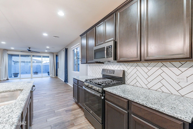 kitchen featuring light stone counters, stainless steel appliances, backsplash, dark brown cabinets, and light wood-type flooring