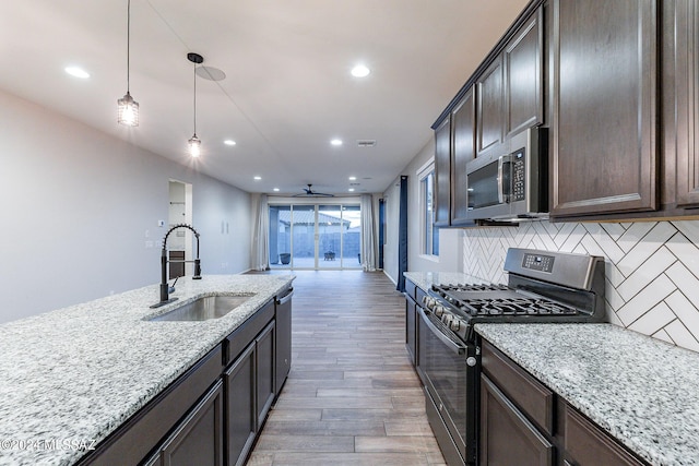 kitchen featuring dark brown cabinetry, tasteful backsplash, light stone counters, stainless steel appliances, and a sink