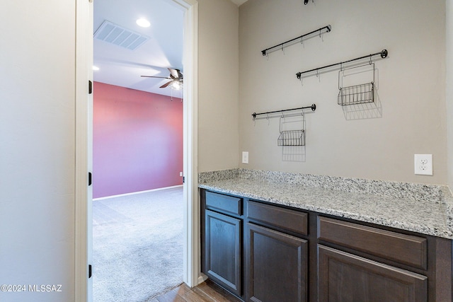 interior space with light carpet, baseboards, visible vents, ceiling fan, and dark brown cabinets