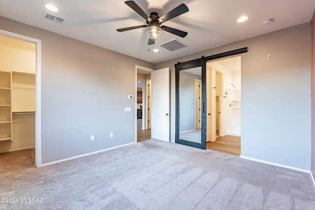 unfurnished bedroom with carpet floors, a barn door, a walk in closet, and visible vents