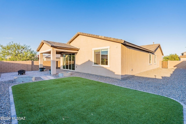 rear view of property featuring an outdoor fire pit, a patio, a fenced backyard, a yard, and stucco siding