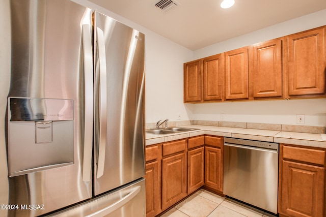 kitchen featuring sink, stainless steel appliances, light tile patterned floors, and tile counters