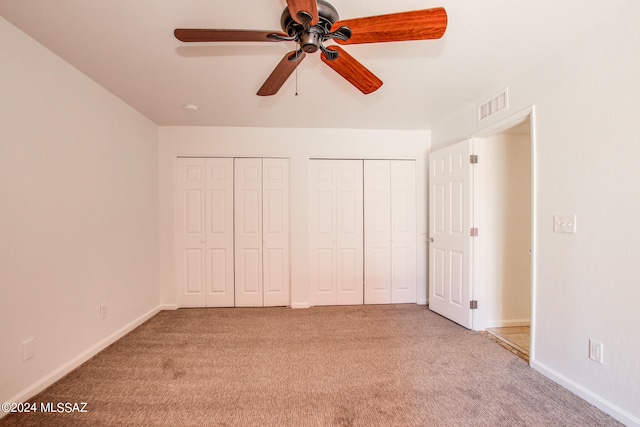 unfurnished bedroom featuring multiple closets, light colored carpet, and ceiling fan